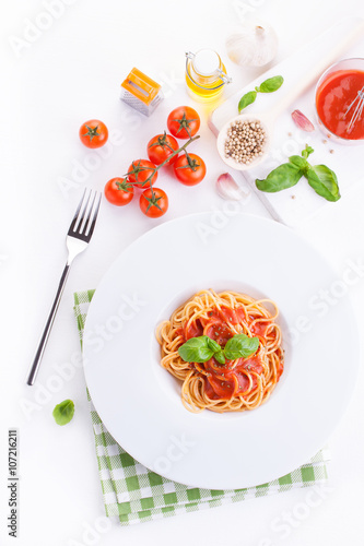 Tomato pasta spaghetti with fresh tomatoes  basil  italian herbs and olive oil in a white bowl on a white wooden background  top view.