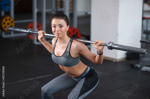 Beautiful young girl engaged in fitness in the gym. Brunette performs exercises with a barbell.