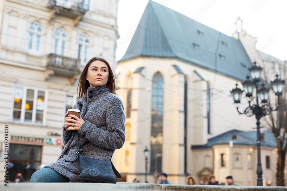 Young stylish woman walking on the street and holding a cup of coffee in her hands.