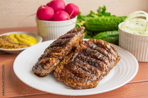 Pork steak, grilled with onion rings and fresh vegetables, herbs