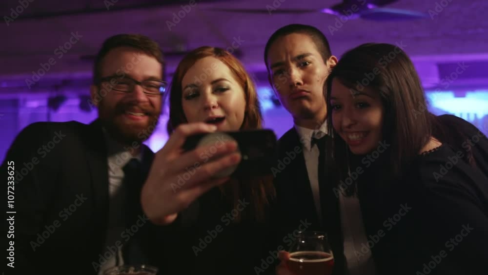 A group of well dressed friends in a nightclub taking selfies with a cell phone A group of well dressed friends in a nightclub taking selfies with a cell phone
