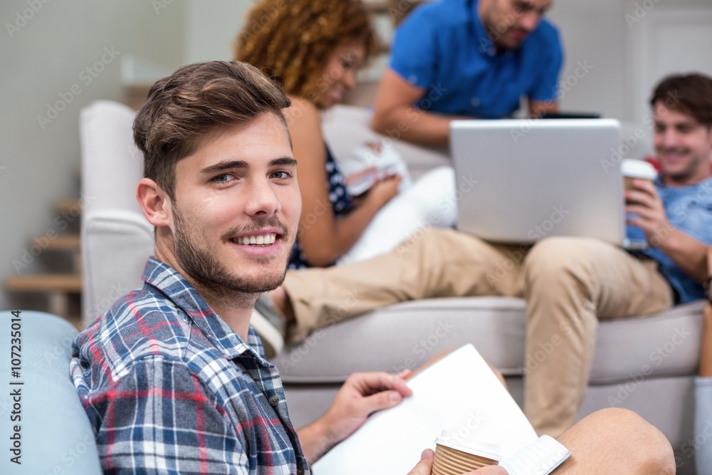 Young man with book while friends in background Young man with book while friends in background