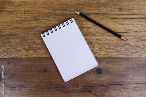 White sheets notebook with spiral in the center of the wooden dark brown table with black pencil on side from above