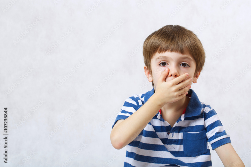 A boy covers his mouth with a palm A boy covers his mouth with a palm