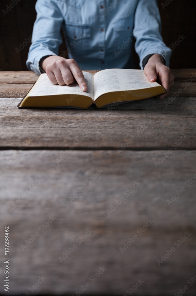 Woman hands praying with a bible in a dark over wooden table Woman hands praying with a bible in a dark over wooden table