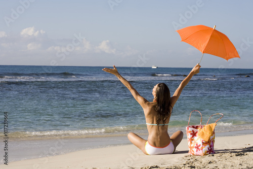 Obraz na plátně femme en maillot de bain assise sur la plage au bord de la mer avec une ombrelle