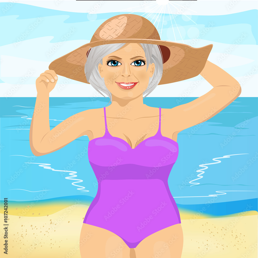 senior woman wearing pink swimsuit and big straw hat at the beach