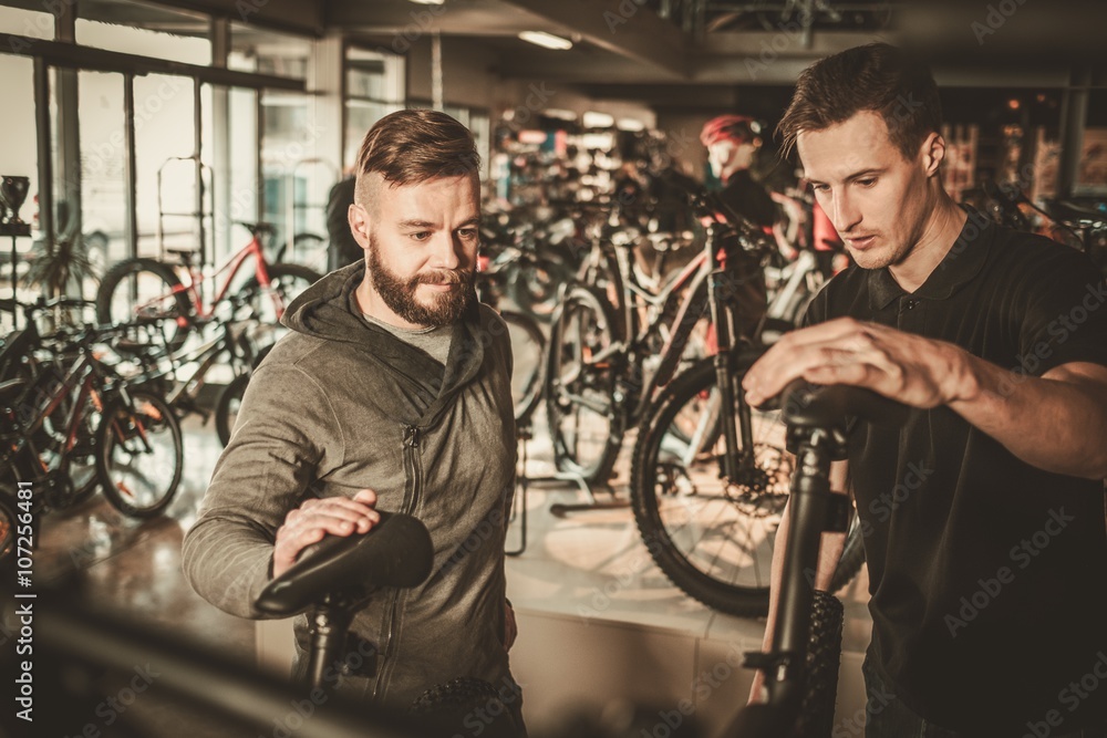 Obraz premium Salesman showing a new bicycle to interested customer in bike shop.