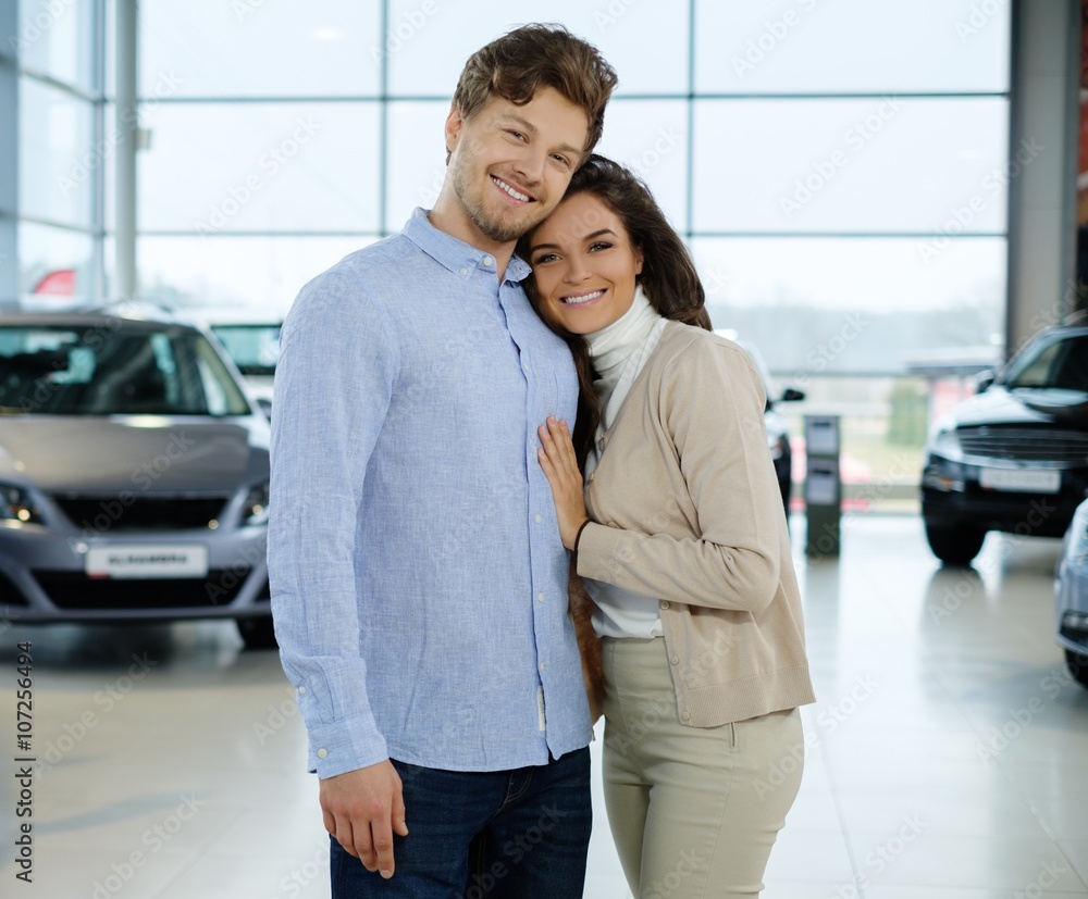 Beautiful young couple looking a new car at the dealership showroom.