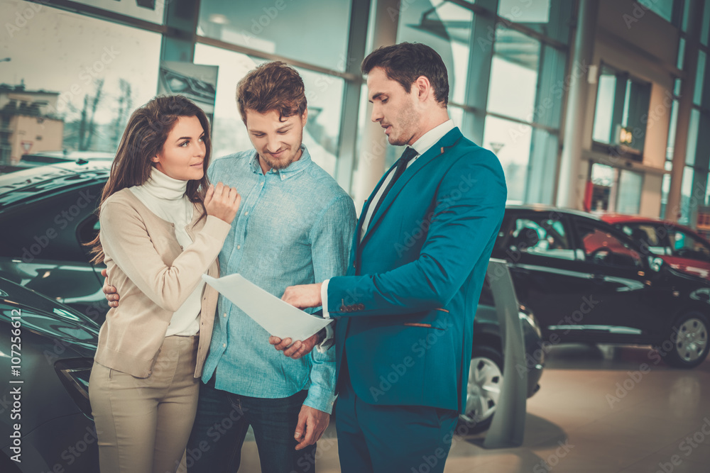 Obraz premium Salesman talking to a young couple at the dealership showroom.