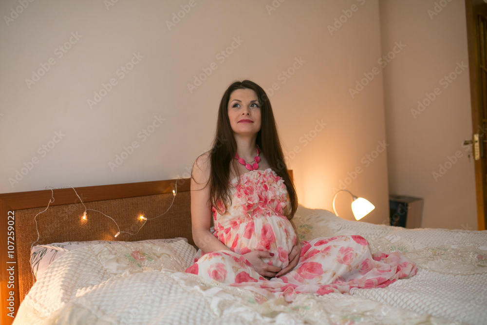 Cute pregnant woman touching her belly while lying on a bed at home Cute pregnant woman touching her belly while lying on a bed at home