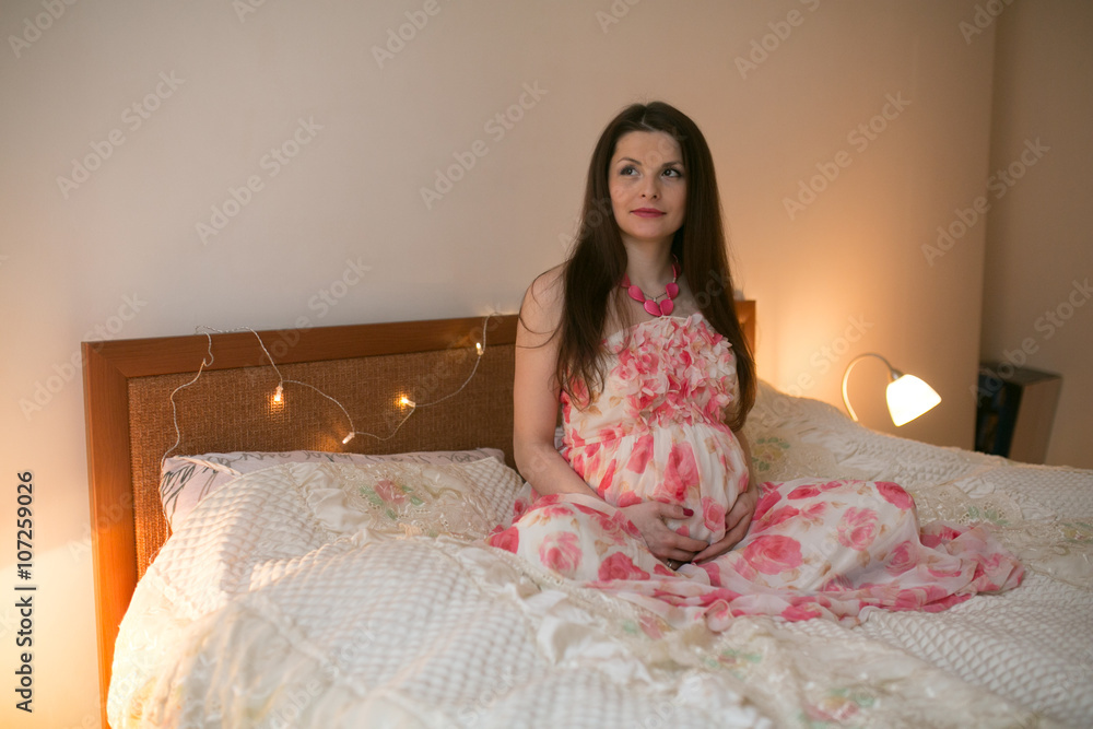 Cute pregnant woman touching her belly while lying on a bed at home Cute pregnant woman touching her belly while lying on a bed at home