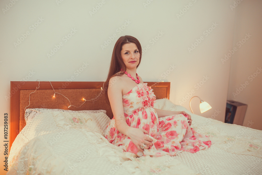 Cute pregnant woman touching her belly while lying on a bed at home Cute pregnant woman touching her belly while lying on a bed at home