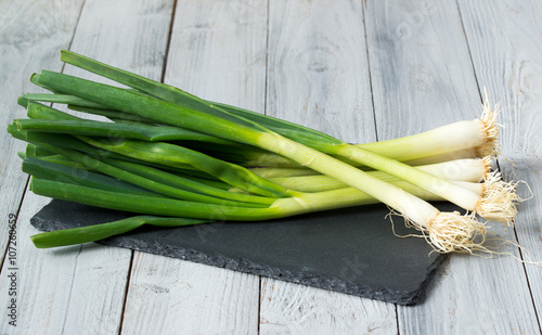 Fresh green onions on the slate cutting board, wooden background