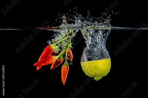 Photos Mezzo limone e mazzo di peperoncini rossi tuffati in acqua su sfondo nero