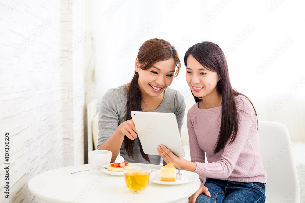 Two woman use of tablet together inside coffee shop Two woman use of tablet together inside coffee shop