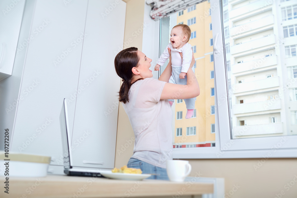 Mom plays with the child at the window in the white kitchen Mom plays with the child at the window in the white kitchen
