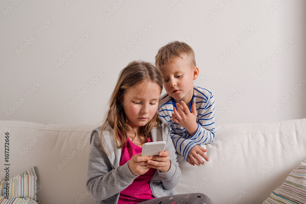 Children at home sitting on sofa, playing with smartphone Children at home sitting on sofa, playing with smartphone