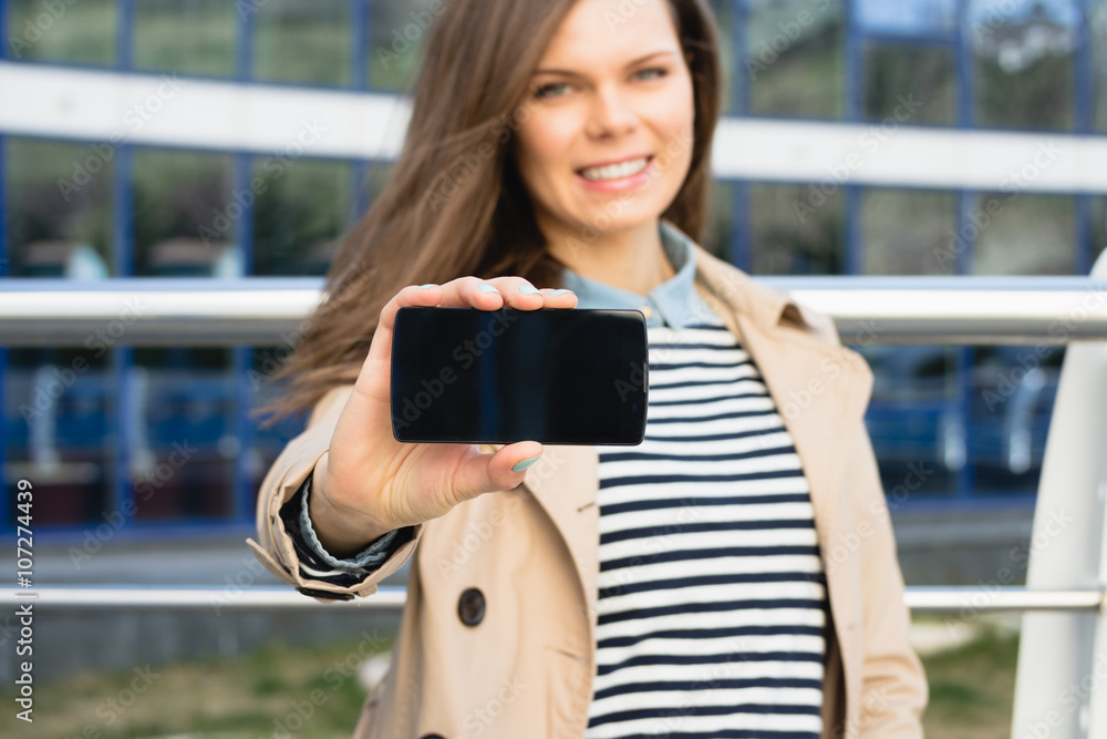 Attractive smiling woman shows the display of the smart phone ou Attractive smiling woman shows the display of the smart phone ou