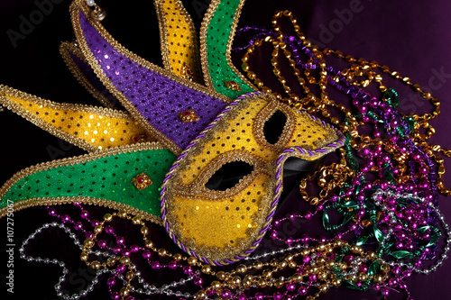 A Mardi gras jester's mask with beads on a black background
