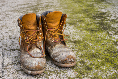 Old worn work boots on grungy dirty ground background photo