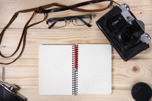 Retro camera with blank notebook on wooden table