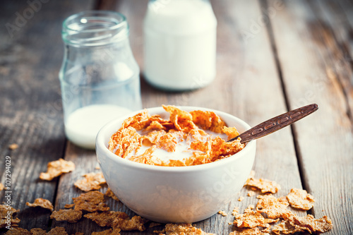 Obraz na płótnie Breakfast cereal wheat flakes in bowl and milk bottles on wooden
