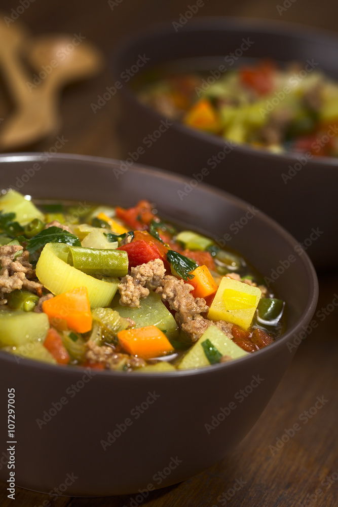 Vegetable soup with mincemeat, green bean, potato, leek, carrot, tomato and parsley served in brown bowls (Selective Focus, Focus in the middle of the soup)