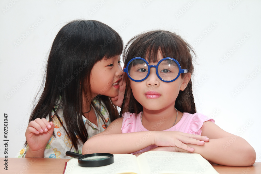 Cute little asian girl whispering something to her sister Cute little asian girl whispering something to her sister