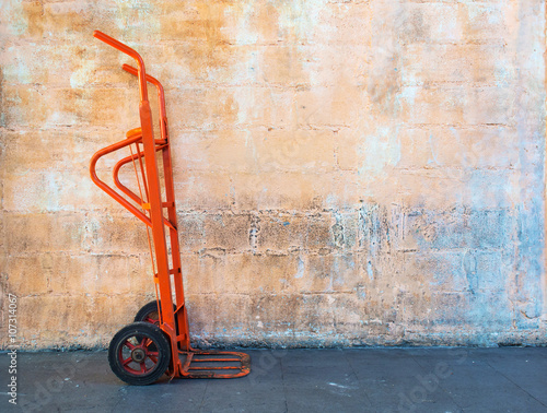 Red steel hand trolley or sack truck against orange brick wall