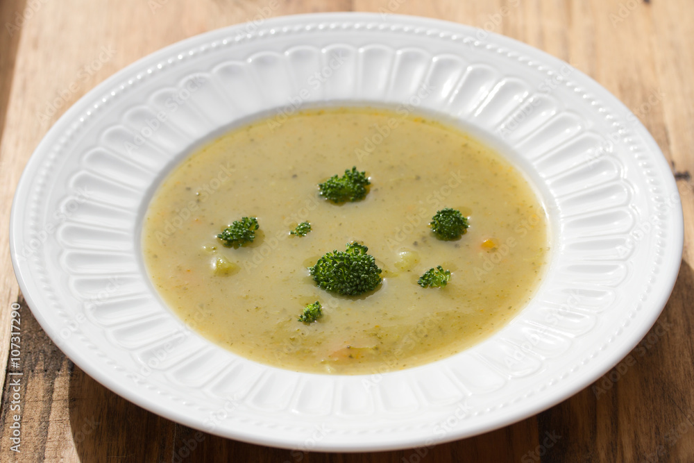 vegetable soup with broccoli on white dish on brown wooden background vegetable soup with broccoli on white dish on brown wooden background