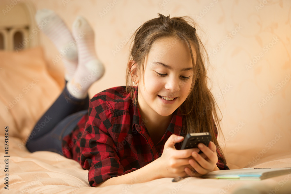 Smiling teenage girl ling on bed and using smartphone Smiling teenage girl ling on bed and using smartphone