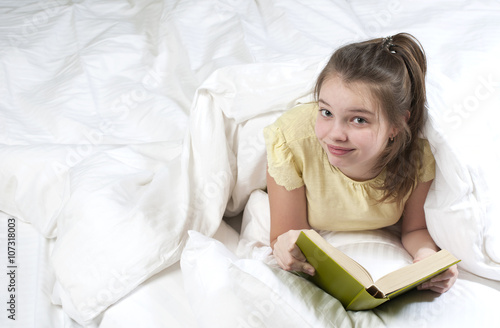 Teenage girl reading a book in bed..