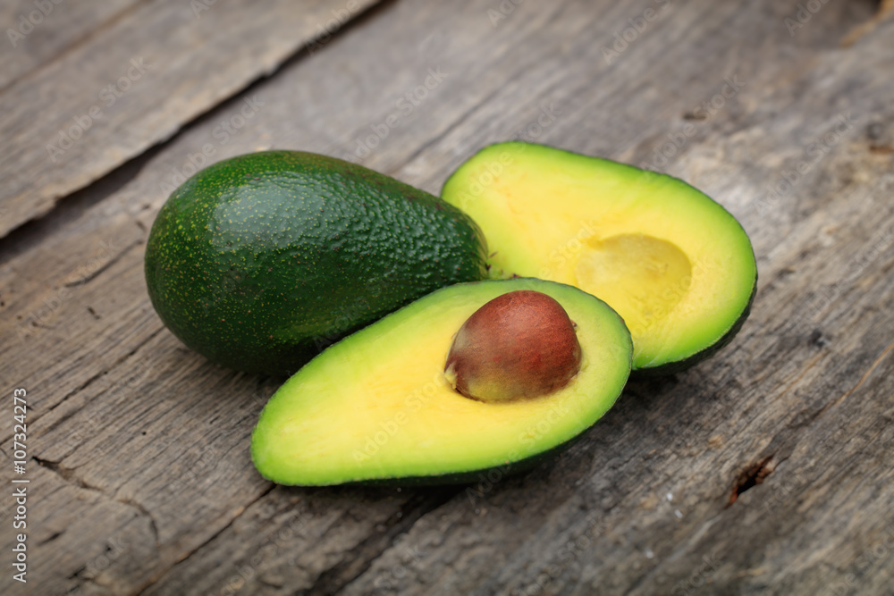 Two avocados one cut in two with seed, on wooden surface Two avocados one cut in two with seed, on wooden surface