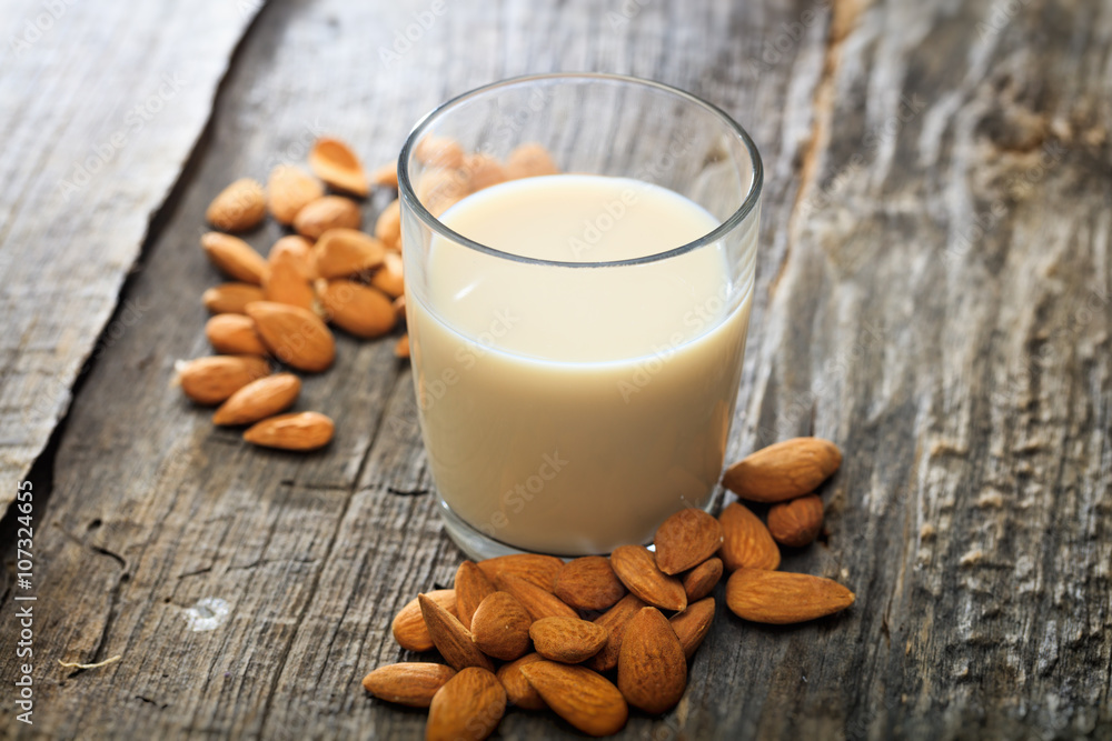 Heap of almonds and a glass of almond milk, on wooden surface Heap of almonds and a glass of almond milk, on wooden surface