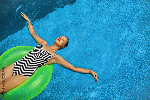 Summer Vacations. Beautiful Sexy Smiling Woman With Perfect Fit Body  Healthy Skin In Swimwear Sunbathing  Floating On Float Swim Ring In Swimming Pool Water. Enjoyment. Beauty  Wellness. Recreation