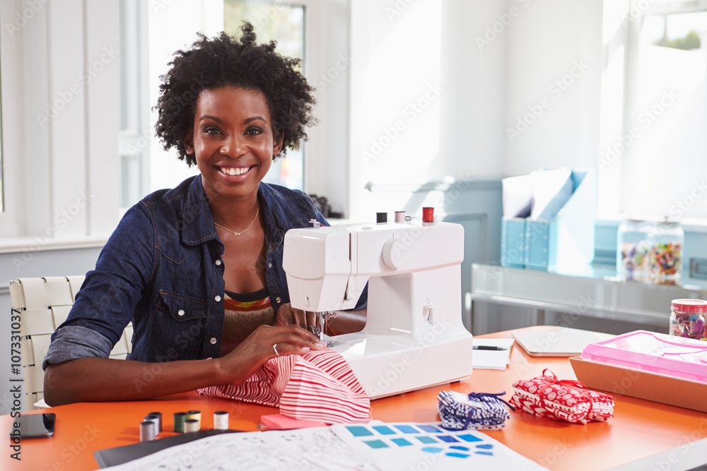 Young black woman using a sewing machine looking to camera Young black woman using a sewing machine looking to camera
