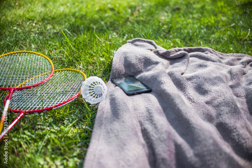 Shuttlecock and badminton racket, mobilephone and Blue picnic blanket on the grass field