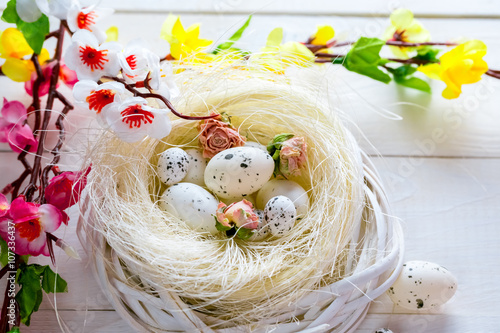 Beautiful Easter background with flowers and nest with eggs on white painted boards