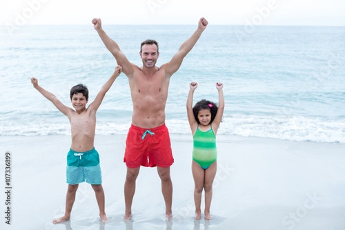 Father and children standing with arms raised at beach