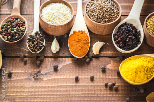 Beautiful colorful spices in wooden spoons and bowls on an old wooden brown table. Free space for your text