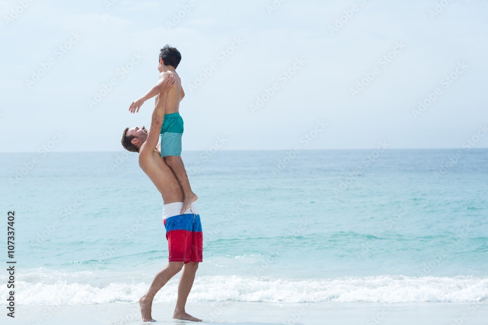 Father carrying son while standing at beach 