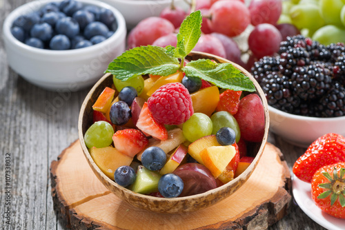Bild auf Leinwand fruit salad in a bamboo bowl and fresh berries, close-up