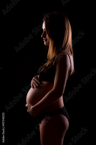 Young pregnant women in black underwear on black background is hugging her tummy