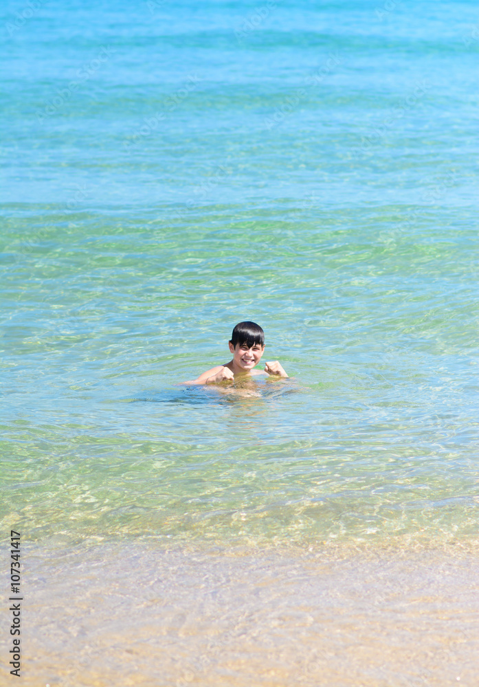 Cute happy young boy smiling into the tropical sea 