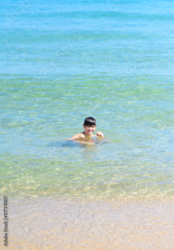 Cute happy young boy smiling into the tropical sea 