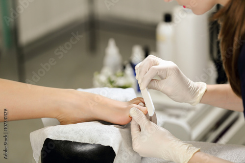 Working with the nail file big toe of clients leg. Service pedicure at the beauty salon.