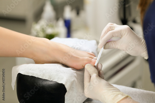 Work with the nail file during pedicure process in beauty salon. Manicurist makes quality service.