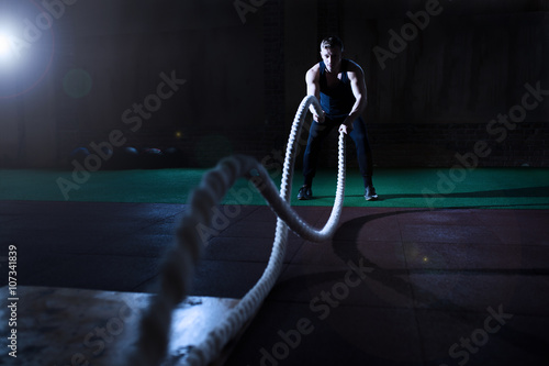 Athletic man doing some crossfit exercises with a rope in gym