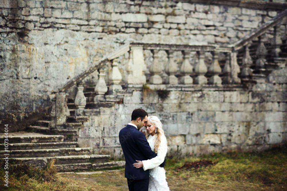 blonde bride and brunette groom walking near  old castle